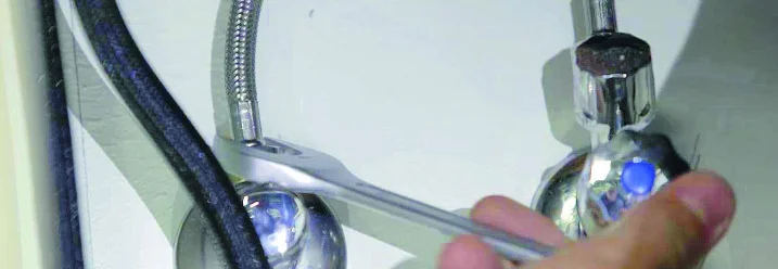 Person montiert mit Schraubenschlüssel einen Wasserhahn.